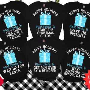 May include: Black t-shirts with holiday-themed graphics. Each shirt features the words "Happy Holidays" above a light blue gift box design. Below the gift box, phrases like "Get Their Tinsel in a Tangle" are printed.
