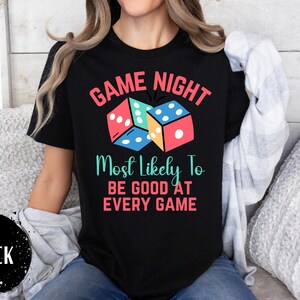 May include: Black t-shirt with the text "Game Night Most Likely To Be Good At Every Game" and a graphic of colorful dice.