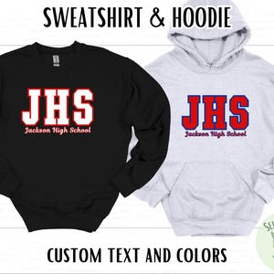 May include: Black sweatshirt and a gray hoodie. Both feature the text "JHS" in red and white, with "Jackson High School" below. The hoodie has a front pocket. The text "SWEATSHIRT & HOODIE" and "CUSTOM TEXT AND COLORS" are also visible.