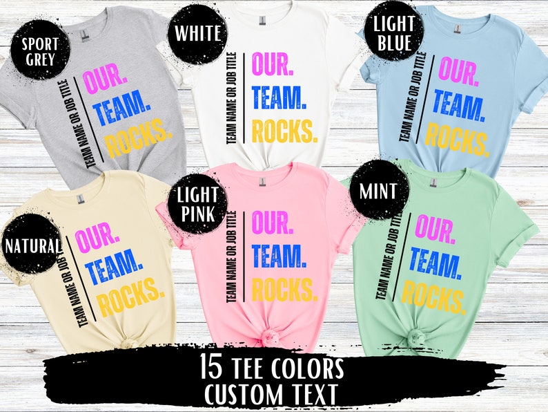 May include: A graphic design for a t-shirt with 15 different color options. The design features the text "Our Team Rocks." in pink, blue, and yellow lettering.