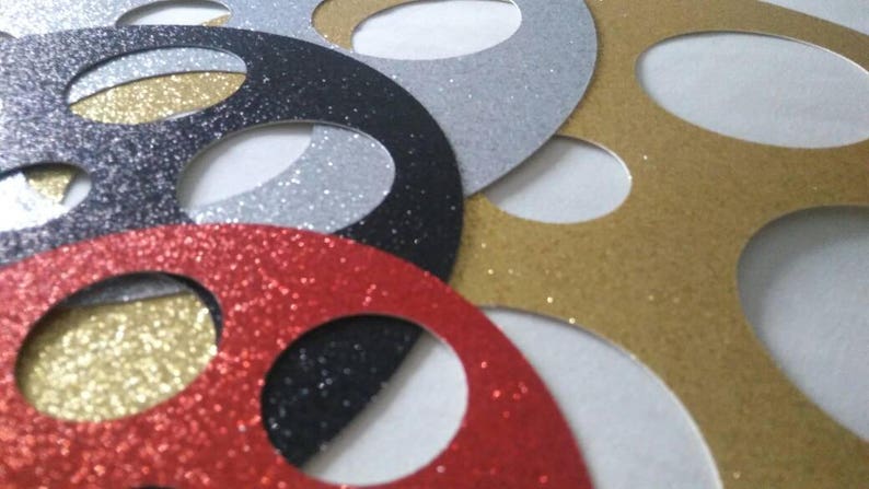 May include: A set of five round, glittery paper circles with cut-out centers. The circles are in red, gold, black, and silver.