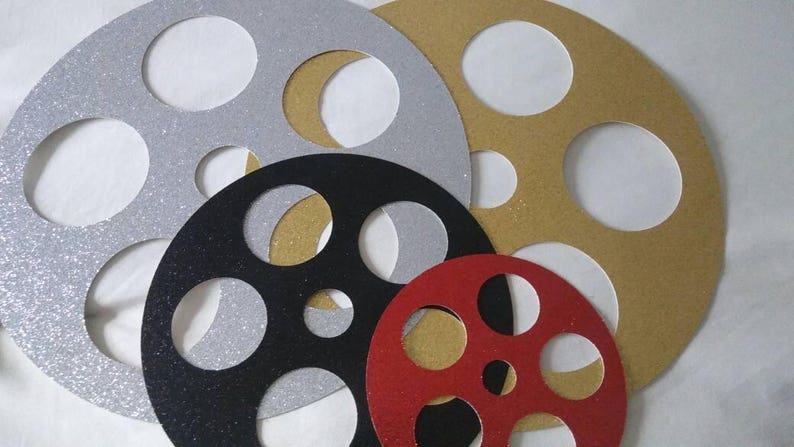 May include: Five different sizes of film reel cutouts, made of glitter paper. The cutouts are in silver, gold, black, and red.