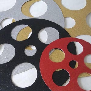 May include: Four decorative film reel shapes, each with a different color and glitter finish. The reels are silver, black, gold, and red.