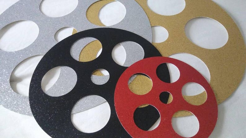 May include: Four decorative film reel shapes, each with a different color and glitter finish. The reels are silver, black, gold, and red.