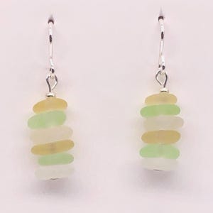 May include: Sea glass earrings with a stack of colorful, rounded sea glass pieces in shades of yellow, green, and white. The earrings hang from silver-colored hooks. The card behind the earrings reads "SEA GLASS VISIONS by Cathy Kelly."