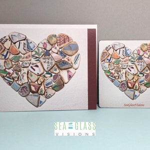 May include: A greeting card and a magnet featuring a heart made of colorful sea glass. The heart is made of many small pieces of sea glass, each with a different color and pattern. The card and magnet are both white with a red border. The text "Sea Glass Visions" is printed on the bottom of the card and the magnet.