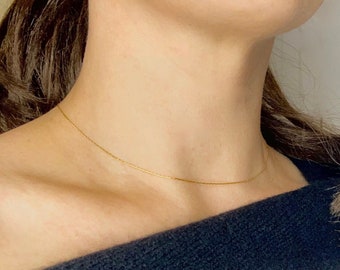 May include: A delicate gold chain necklace worn on a person's neck. The chain is thin and simple, and it is a popular choice for everyday wear.
