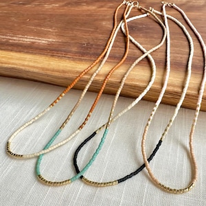 Puede incluir: Cuatro collares de cuentas con detalles dorados. Los collares están hechos con cuentas de diferentes colores, incluyendo blanco, naranja, negro y turquesa.
