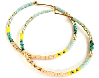 May include: A pair of large hoop earrings with a multi-colored beaded design. The beads are light blue, turquoise, yellow, and beige.