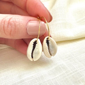 May include: Gold hoop earrings with white cowrie shell charms. The shells are smooth and have a natural, organic look.