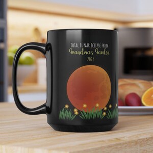 May include: Black ceramic coffee mug with a graphic of a red moon and the text "Total Lunar Eclipse from Grandma's Garden 2025".