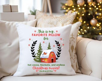 May include: White square pillow with the text "This is my FAVORITE PILLOW for hot cocoa, blankets, and endless Christmas movies! Samantha." The pillow has a graphic of a red house with snow on the roof and two green trees.