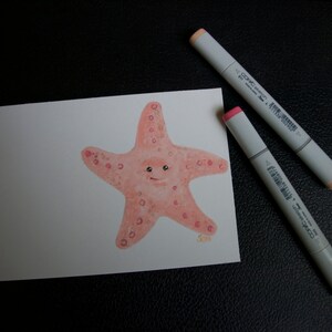 May include: A watercolor illustration of a smiling starfish in shades of peach and pink, with darker pink spots. Two gray and peach-colored Copic Sketch markers are positioned diagonally across the image, adding a touch of artistic flair.