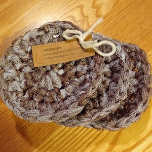 May include: Three crocheted coasters in brown and white with a gold shimmer. The coasters are tied together with a white string. A small brown tag with the text "HdcDesigns www.HdcDesigns.Etsy.com jodidejonge@gmail.com" is attached to the string.