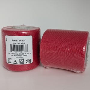 May include: Two rolls of red nylon net yarn, each wrapped in clear plastic. The label on one roll reads "RED NET 3 IN X 40 YDS." The yarn is made in the USA of imported yarn. The rolls are cylindrical and have a textured appearance.