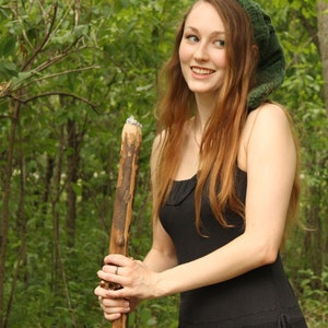 May include: A woman with long red hair wearing a green knitted hat and a black dress holds a wooden walking stick.