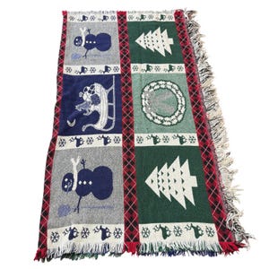 Pode incluir: Uma manta retangular com tema natalino com um design de patchwork. A manta apresenta quadrados com imagens de bonecos de neve, árvores de Natal e coroas. O esquema de cores inclui azul marinho, verde, cinza e detalhes em vermelho. A manta tem uma borda com franjas.