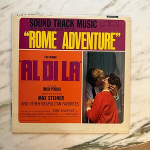 May include: Vintage vinyl record album cover for the soundtrack of "Rome Adventure." The cover features text in purple and orange, including "Rome Adventure" and "Al Di La." A photo of a couple kissing is on the right side of the cover.