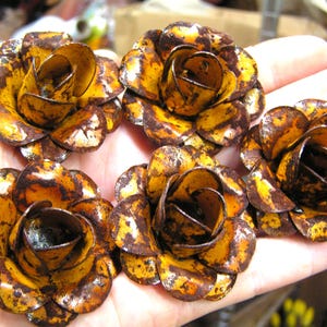 Puede incluir: Cinco adornos de metal con forma de rosa, cada uno con un acabado amarillo brillante y manchas de color marr&oacute;n oscuro que parecen &oacute;xido en los p&eacute;talos superpuestos. Estas piezas florales decorativas tienen una estructura redondeada y multicapa.
