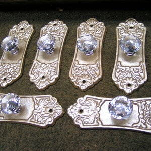May include: Set of seven antique-style door knobs. Each knob features a clear, faceted crystal ball mounted on a decorative, ornate, gold-colored backplate. The backplates have a floral design and are in various shapes.