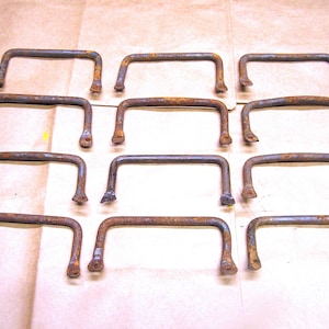 May include: Twelve rusty metal handles with a rectangular shape. The handles are arranged in four rows of three.