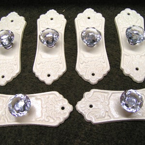 May include: Six white ceramic drawer pulls with ornate designs and clear crystal knobs.