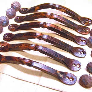 May include: Set of eight rustic iron cabinet pulls with a twisted design and a hammered finish. The pulls are approximately 4 inches long and have two holes for mounting. The set also includes eight matching hammered iron knobs.