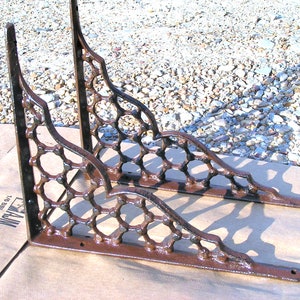 May include: Two ornate metal shelf brackets with a decorative, geometric design. The brackets are a rusty brown color and have a distressed finish.