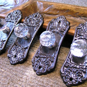 May include: Four black cast iron drawer pulls with ornate designs and clear crystal knobs.