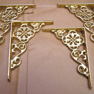May include: Four gold metal corner brackets with a decorative floral design. The brackets are ornate and have a vintage look.