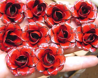 Puede incluir: Una colección de diez rosas de metal rojo con detalles dorados. Las rosas están dispuestas en un patrón circular en una mano.