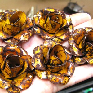 Puede incluir: Cinco adornos de flores de metal con forma de rosa. Cada flor presenta un color base amarillo brillante con manchas de color marr&oacute;n oscuro que parecen &oacute;xido y texturas desgastadas que cubren los p&eacute;talos curvos de las flores.