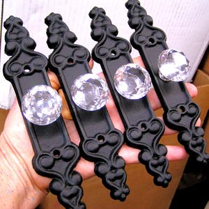 May include: Five black metal drawer pulls with ornate designs and clear glass crystal knobs.