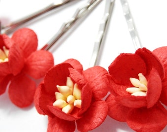 Op de afbeelding: Vier rode papieren bloemen haarclips met zilveren metalen haarspeldjes. De bloemen hebben een gele kern.