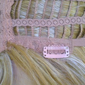 May include: The back of a blonde wig with a lace front and adjustable straps. The wig has clips to secure it to the wearer's hair.