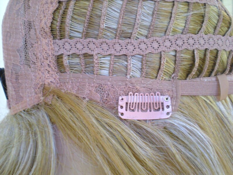 May include: The back of a blonde wig with a lace front and adjustable straps. The wig has clips to secure it to the wearer's hair.