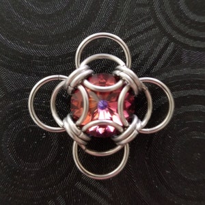 May include: A silver metal flower charm with a pink and purple gemstone in the centre.