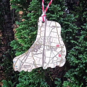 Op de afbeelding: Een witte papieren ornament in de vorm van een laars met een gedrukte kaart van Sedgwick, Engeland. De ornament hangt aan een rood-wit touwtje.