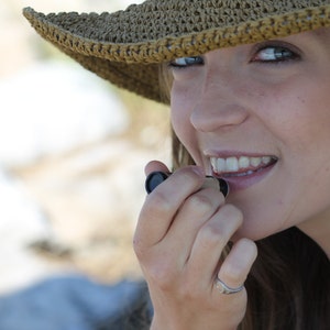 Puede incluir: Una mujer con un sombrero de paja tejido marr&oacute;n se aplica b&aacute;lsamo labial con la mano derecha.