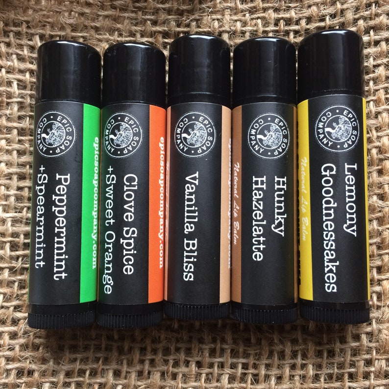Puede incluir: Seis tubos de b&aacute;lsamo labial negros con etiquetas y aromas de diferentes colores. Los aromas son Lemony Goodnessakes, Hunky Hazelatte, Vanilla Bliss, Clove Spice, Sweet Orange y Peppermint.