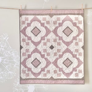 Peut inclure: Une courtepointe rose et marron avec un motif géométrique. La courtepointe est faite de carrés et de diamants, et elle a un fond blanc.