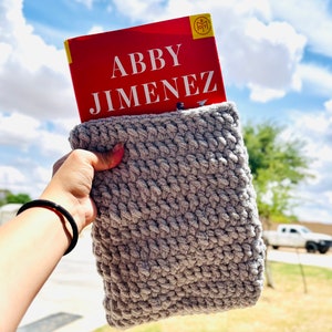 May include: A gray crocheted book sleeve with a red book titled "Abby Jimenez" inside.