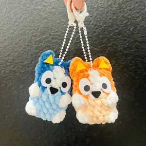 May include: Two plush keychain characters, one blue and one orange, with big eyes and a smiling expression. They are attached to a white keychain.