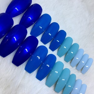 Puede incluir: Conjunto de uñas postizas de presión azul y azul claro degradado. Las uñas son largas y de forma de ataúd. Las uñas están dispuestas en un degradado de azul oscuro a azul claro.