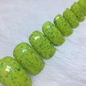 May include: A set of ten green oval-shaped press-on nails with a light green base and gold and green glitter.