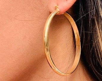 May include: Gold hoop earrings. The earrings are large and circular, with a smooth, polished finish.