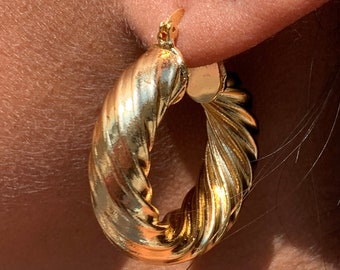 May include: Gold hoop earrings with a twisted design. The earrings are worn in a person's ear.