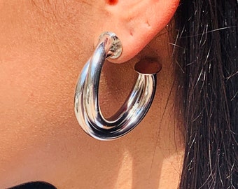 May include: Silver hoop earrings with a twisted design. The earrings are large and have a polished finish.