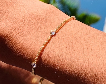 May include: A delicate gold chain bracelet with small clear gemstones. The bracelet is on a person's wrist.