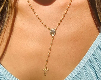 Puede incluir: Un collar de cadena dorada con un pequeño colgante redondo y un dije de cruz.